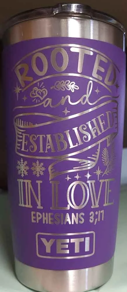 A purple tumbler with gold text and decorative designs featuring a Bible verse from Ephesians 3:17 about love and faith in Yeti.