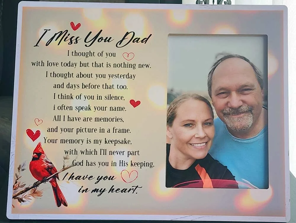 A framed memorial card for a father featuring a photo of a smiling man and woman, a poem titled 'I Miss You Dad', with red and pink hearts, a red cardinal bird illustration, and soft bokeh background.