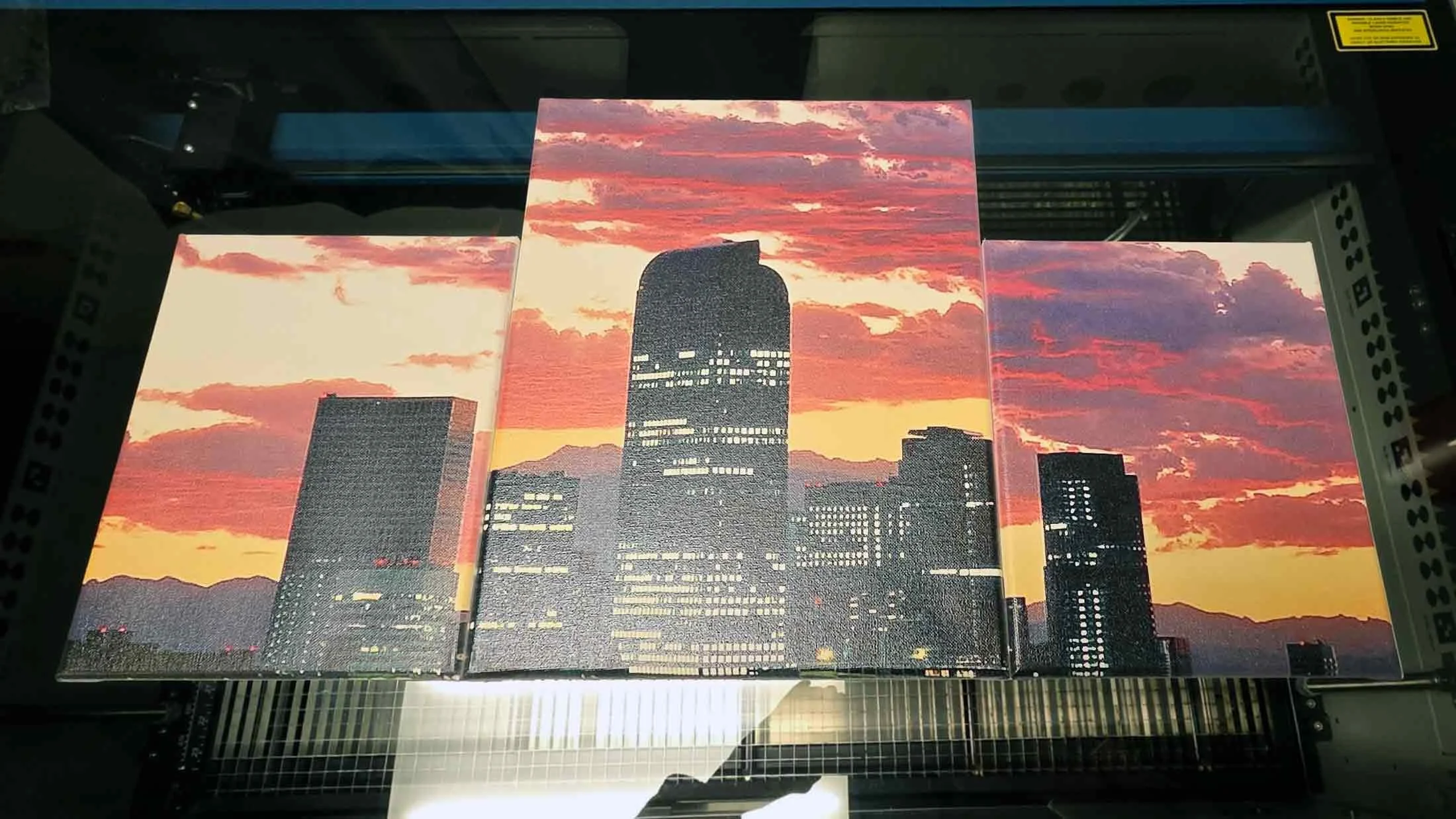 Three canvases or panels displaying a city skyline at sunset, with illuminated skyscrapers and a sky filled with red, orange, and purple clouds.