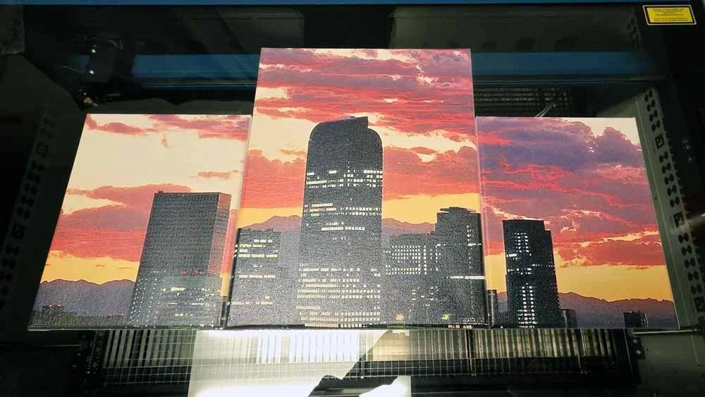 Multilayer illuminated canvas print of a city skyline at sunset, displaying tall buildings and pink-orange clouds.