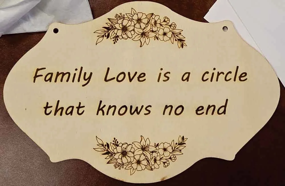 A decorative sign with a floral border at the top and bottom, displaying the quote: 'Family Love is a circle that knows no end' in brown lettering.