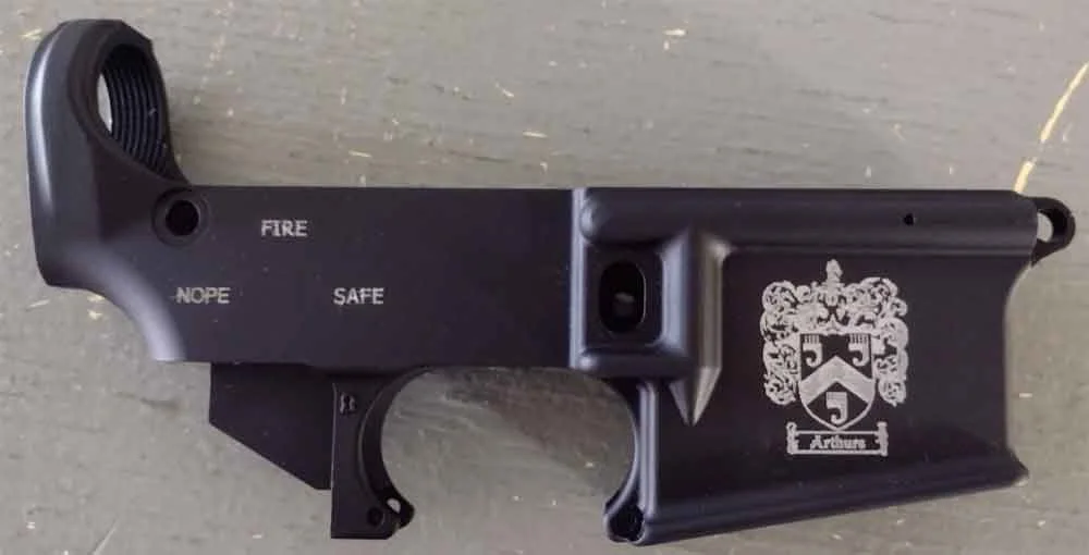 Black firearm with a white crest and text reading 'Arbour' on the grip, lying on a wooden surface.