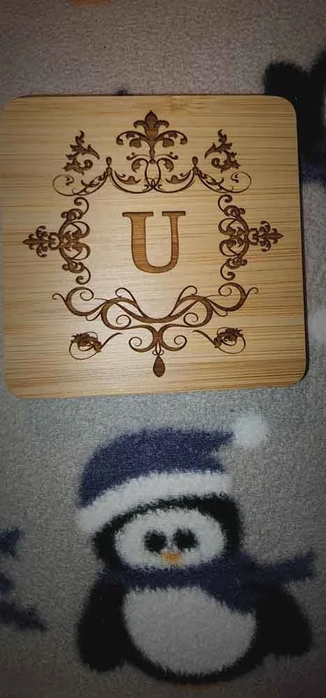 A wooden board with an ornate engraved letter 'U' and decorative flourish design, placed on a penguin-patterned carpet.
