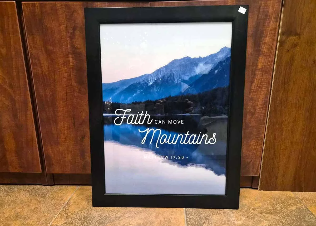 Framed picture featuring a scenic mountain landscape with a lake in the foreground. Overlaid text reads, "Faith Can Move Mountains" and references Matthew 17:20.