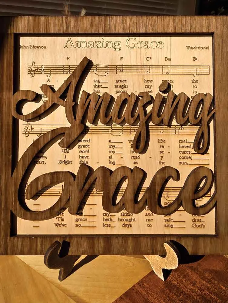 A wooden decorative sign with the phrase "Amazing Grace" and the words "Amazing Grace" in large cursive letters overlaid on sheet music.