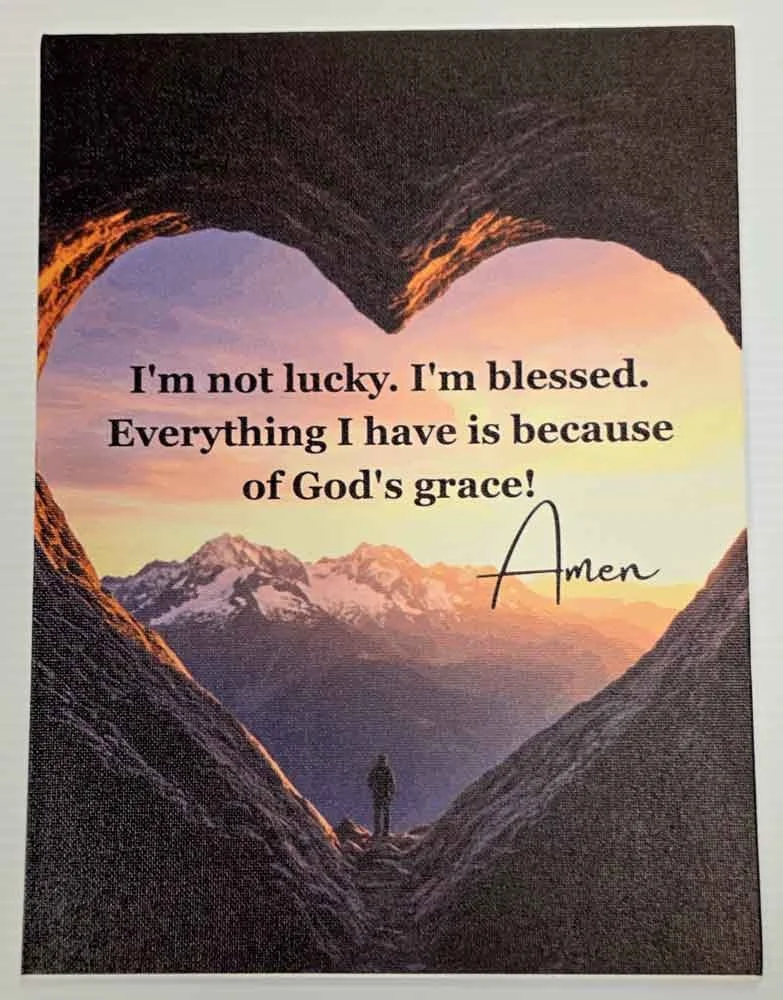 A person standing in a mountain valley framed by a heart-shaped opening in rocks, with snow-capped mountains in the background and a sunset sky