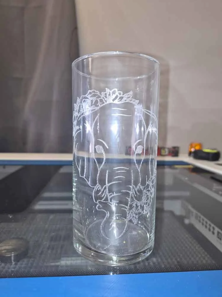 Clear glass tumbler with etched elephant design on the front, placed on a glass surface.