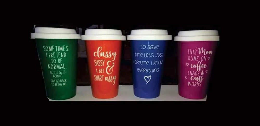 Four colorful coffee cups with humorous quotes on a shelf.