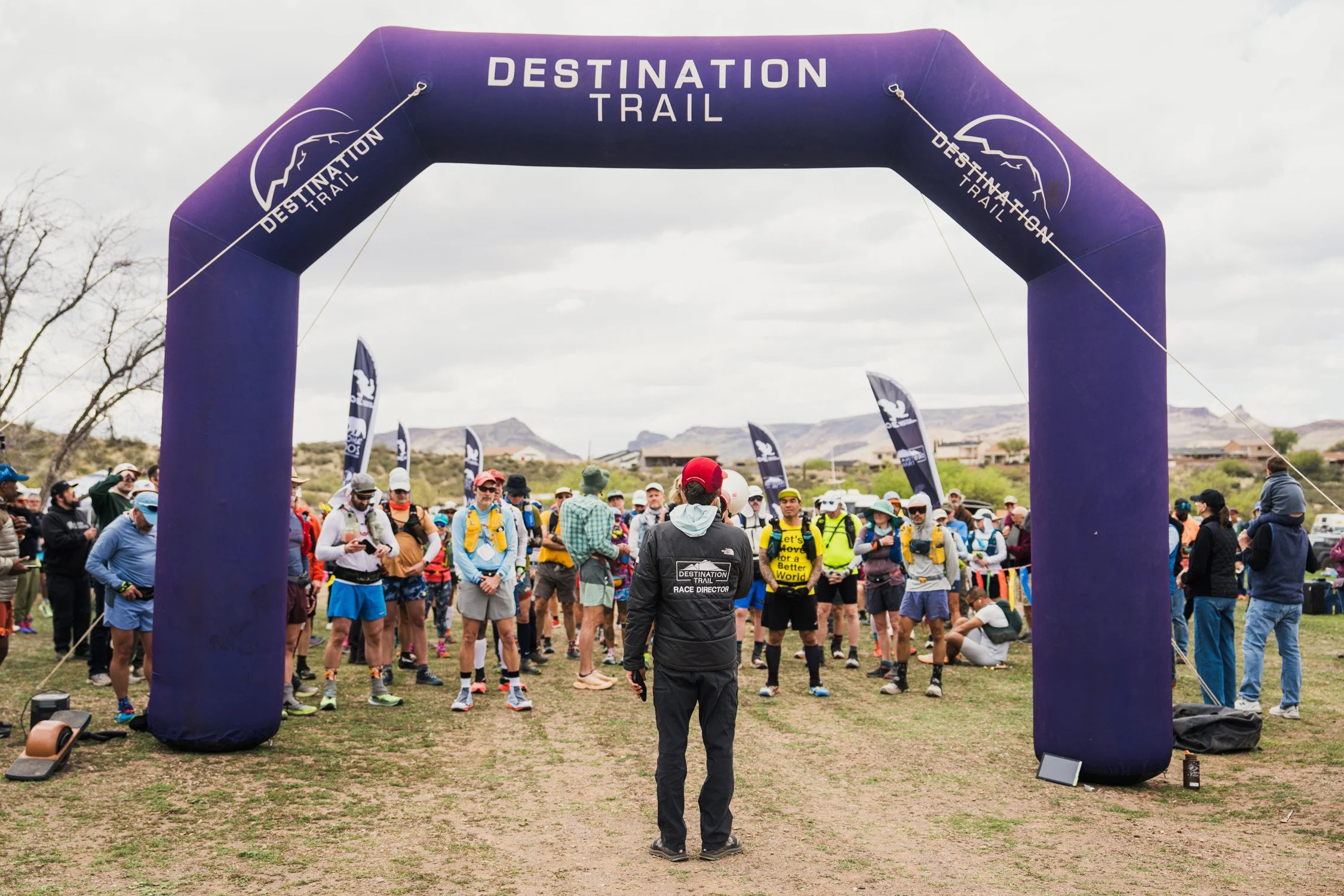 Group of people gathered at the starting line of a Destination Trail race under an inflatable arch with mountain scenery in the background
