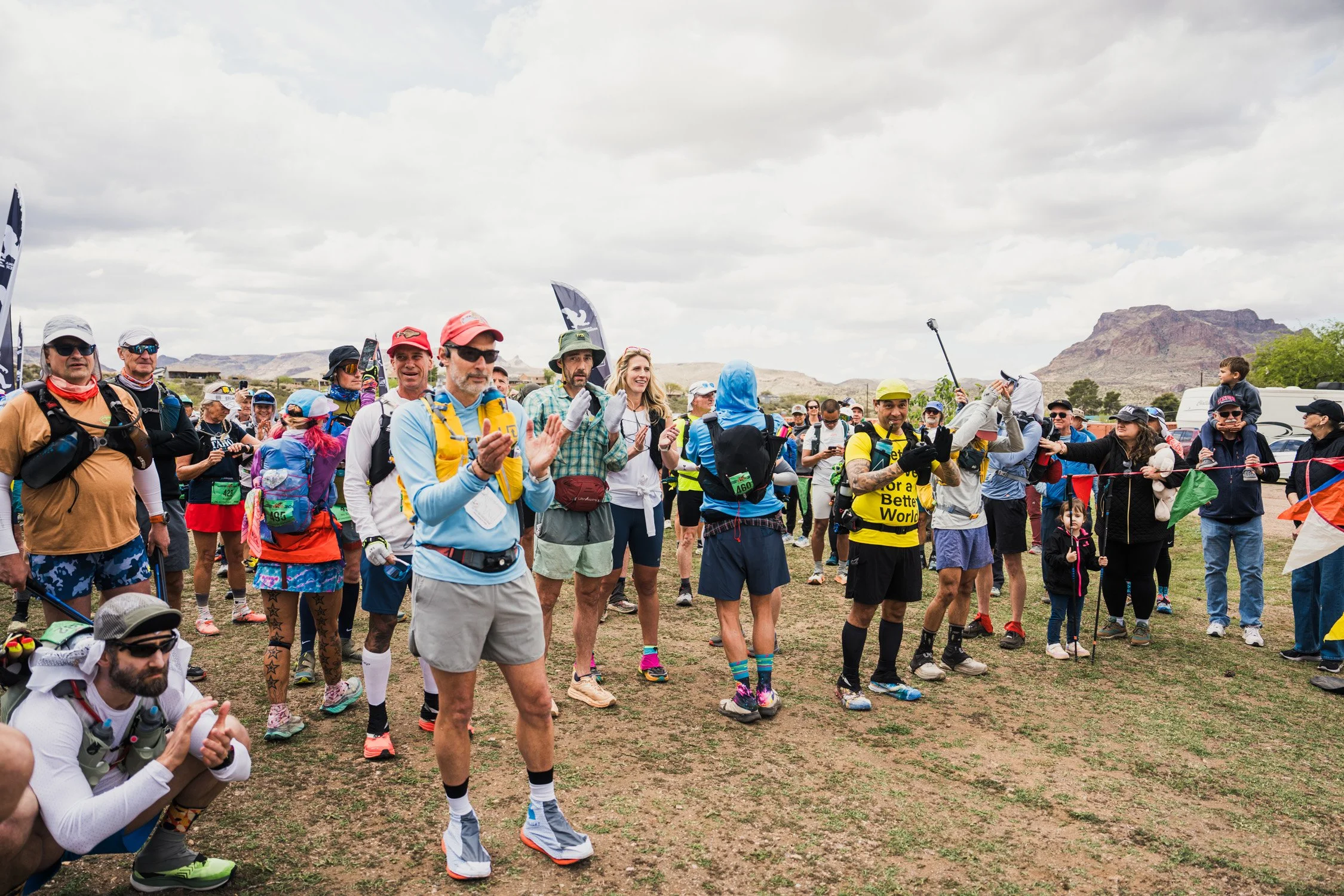 Group of marathon runners gathering at the starting line under cloudy sky with mountainous desert background