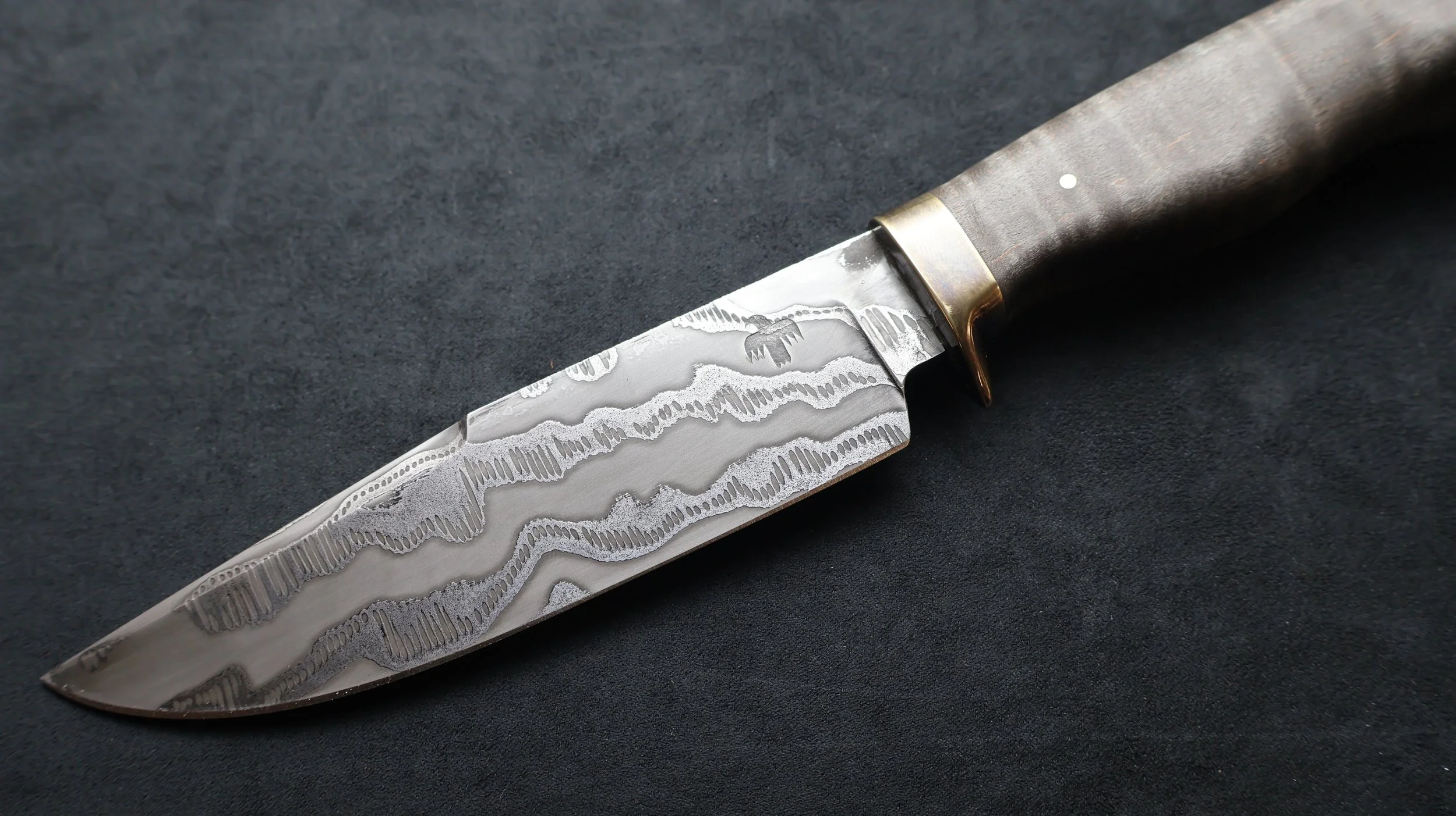 A close-up of a Damascus steel hunting knife with a patterned blade and wooden handle on a black surface.