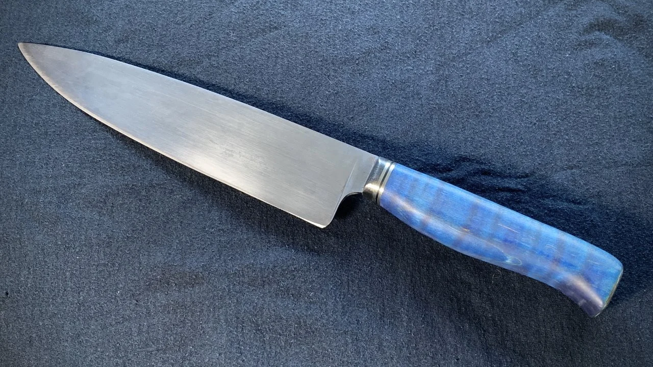 A chef's knife with a blue curly maple handle made by Monty Wheeler at 66Forge.com