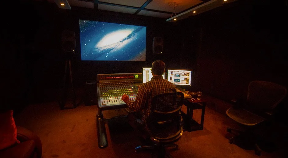 A sound engineer working at a mixing console in a recording studio with a large screen displaying a galaxy image.