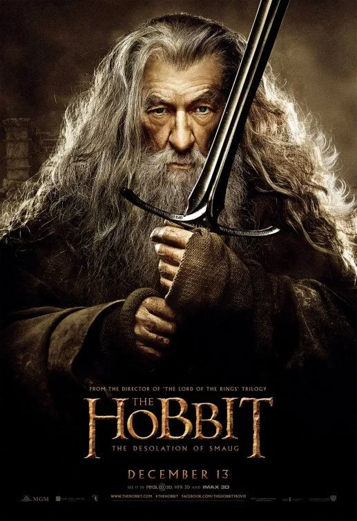 A promotional poster for the movie 'The Hobbit: The Desolation of Smaug' featuring an older man with long gray hair and beard, holding a sword with a serious expression.