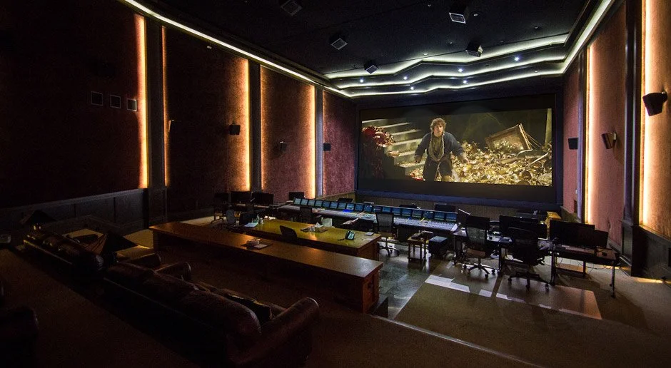 A luxurious movie theater with plush red seating, multiple rows of chairs with armrests, a large screen displaying a scene from a movie, and ambient lighting on dark walls.