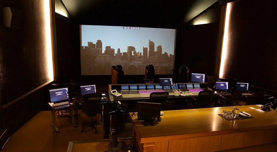 Recording studio control room with sound mixing console, multiple monitors, and a large screen displaying a city skyline.