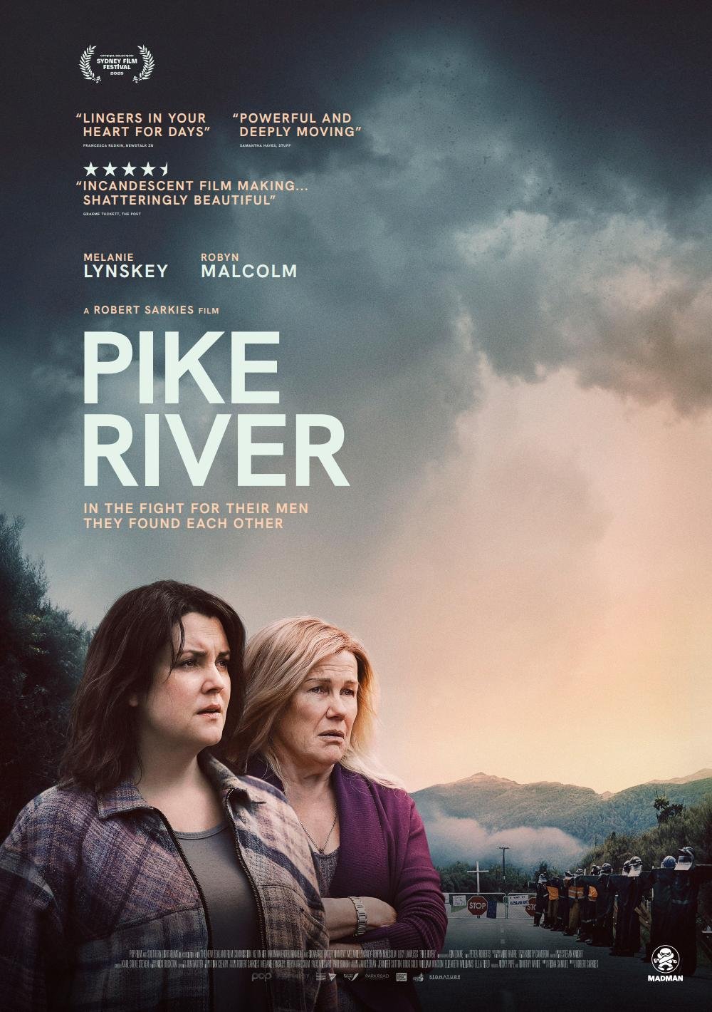 The movie poster for Pike River features two women standing with their arms crossed, looking serious, against a backdrop of dark clouds and distant mountains. Below them, police officers and onlookers gather near a road, with armed police present. The poster includes quotes, actor names, a film title, and festival recognition.