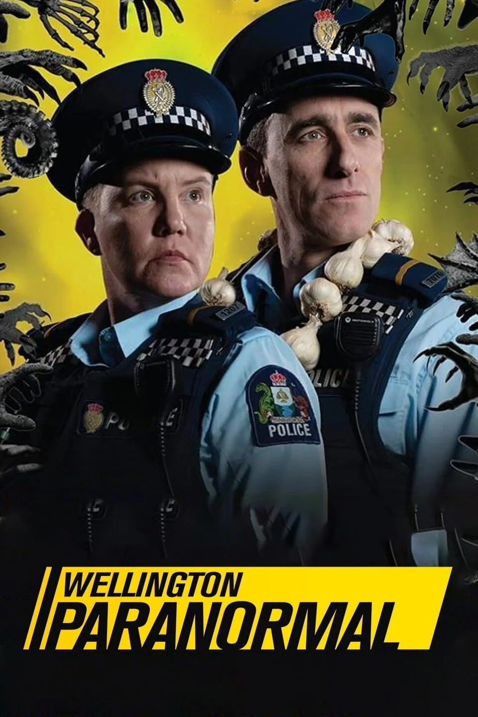 Two male police officers in uniform with police badges and patches, wearing hats, posed with serious expressions against a yellow background with dark hands reaching toward them and ghostly arms around their shoulders. The text reads "Wellington Paranormal" in bold yellow and black font.