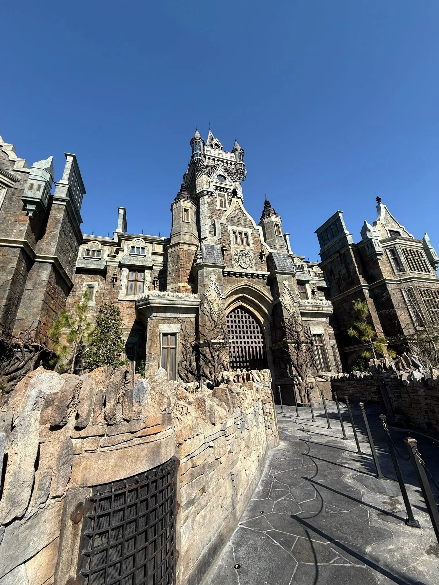 A castle with gothic architecture featuring tall towers, pointed spires, and detailed stonework, set against a clear blue sky.