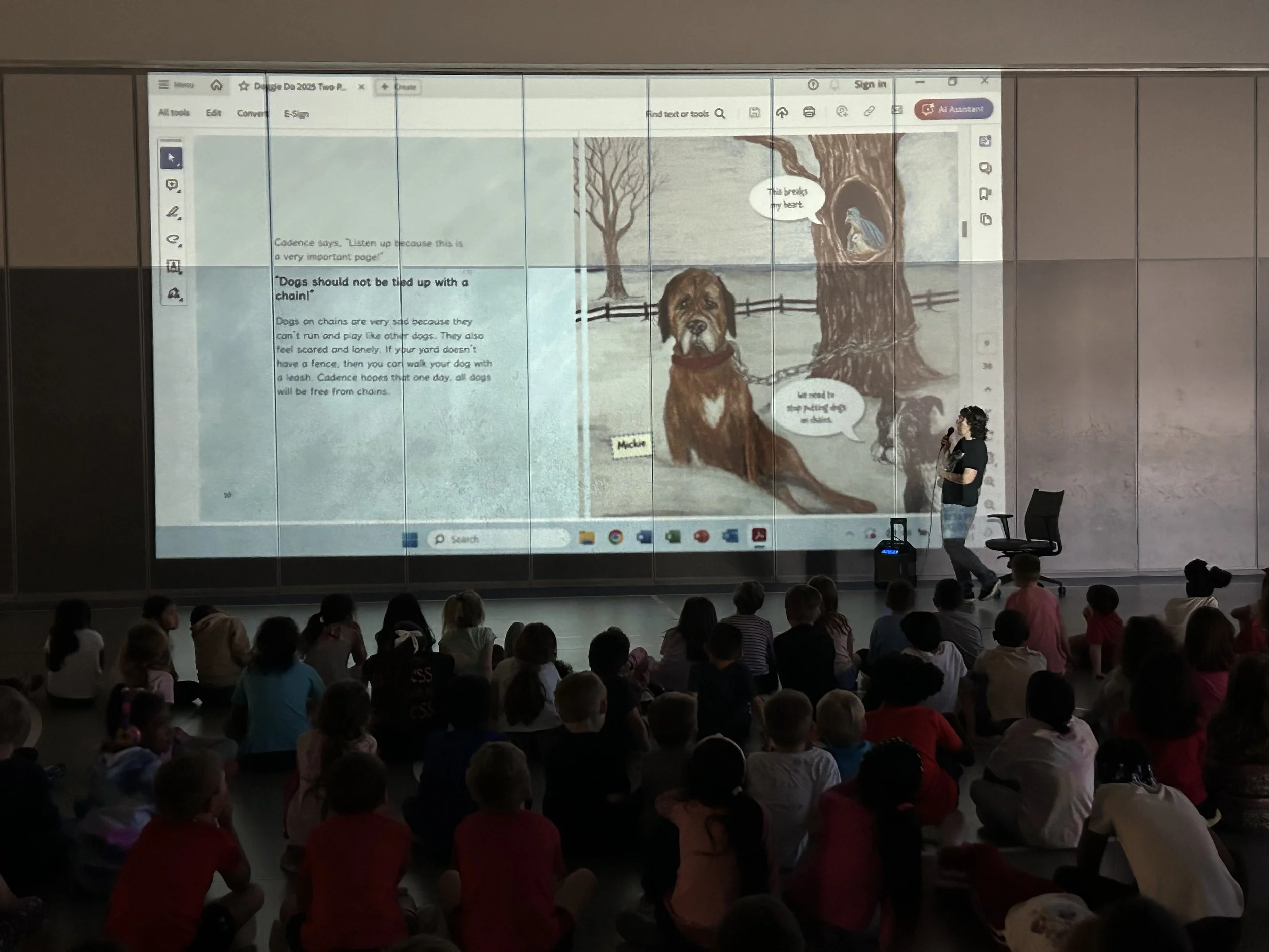 Author in front of audience of children with book pages displayed on large screen