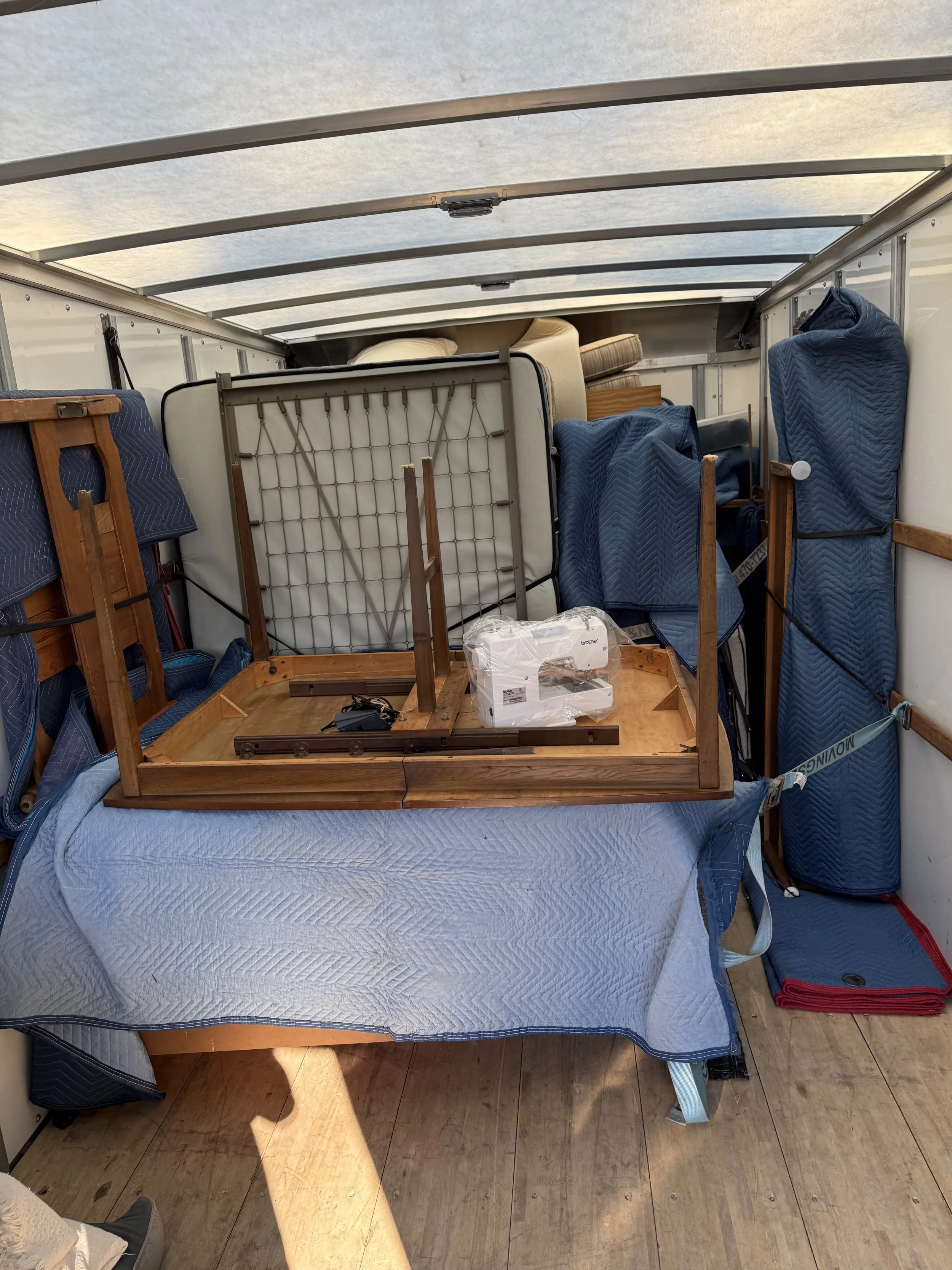 Interior of a moving truck packed with furniture, including a glass table upside down, mattresses, and blue moving pads.