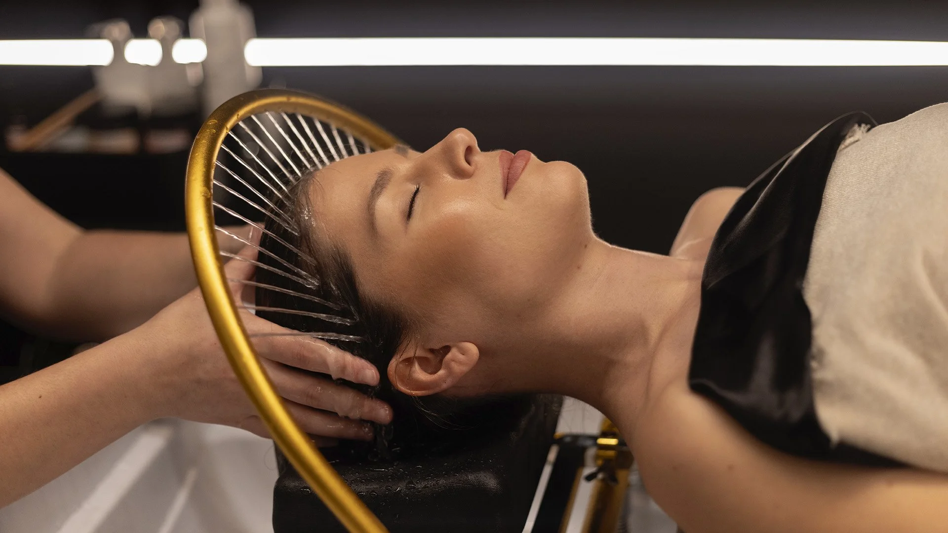 Une femme reçoit un spa de tête dans un salon de coiffure, elle est allongée avec les yeux fermés et une personne lui masse le cuir chevelu. Dans un commerce de Longueuil.