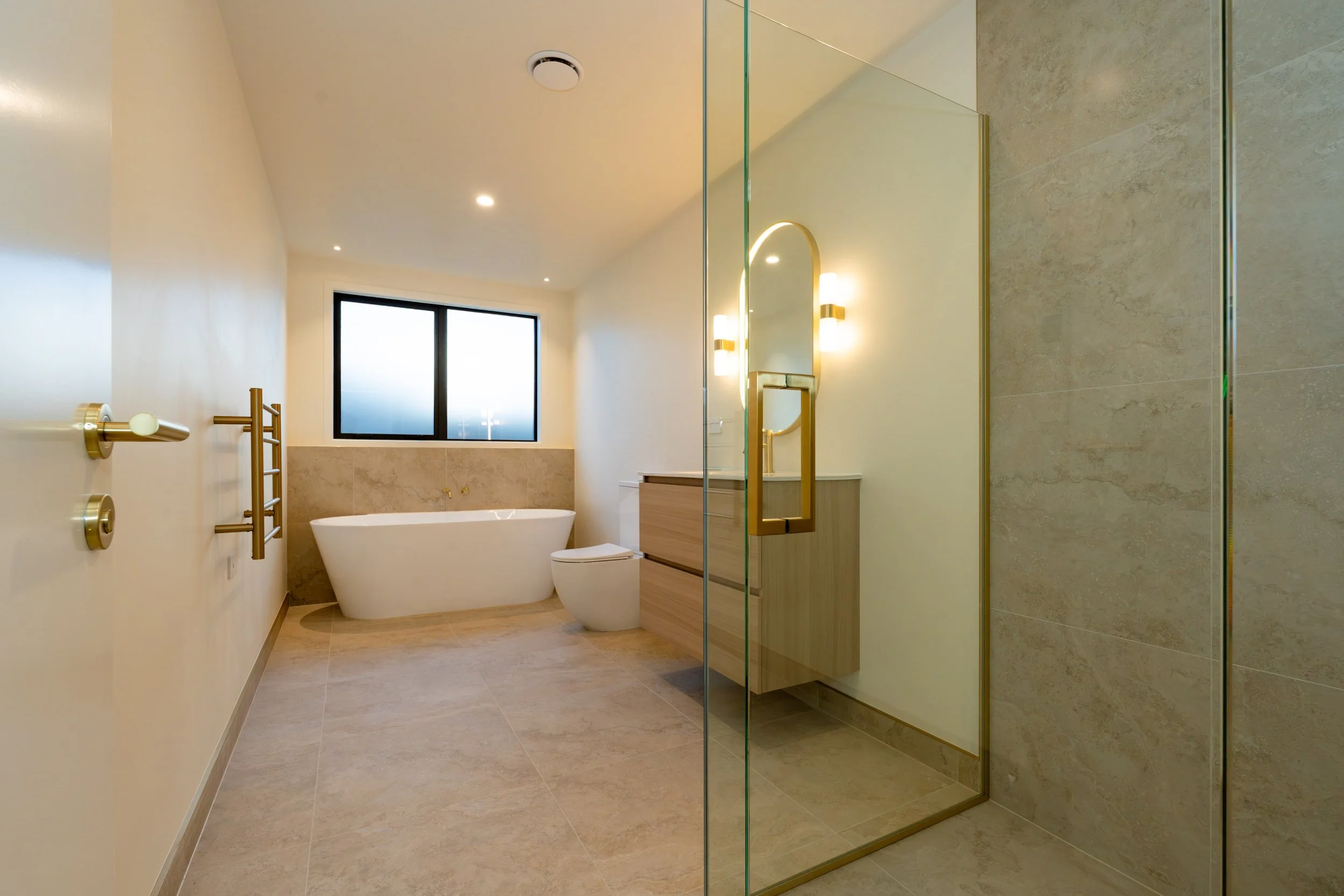 Contemporary main bathroom featuring a floating vanity, premium brass tapware, large-format tiles and timeless finishes in a custom Queenstown home by Adept Carpentry.