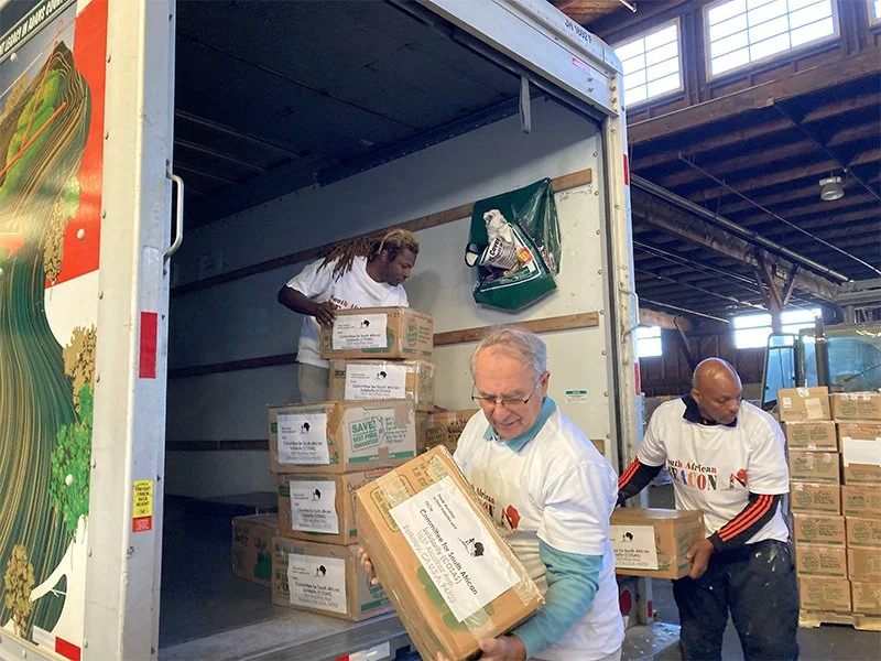 Three volunteers unloading boxes of school supplies onto pallets for the shipment
