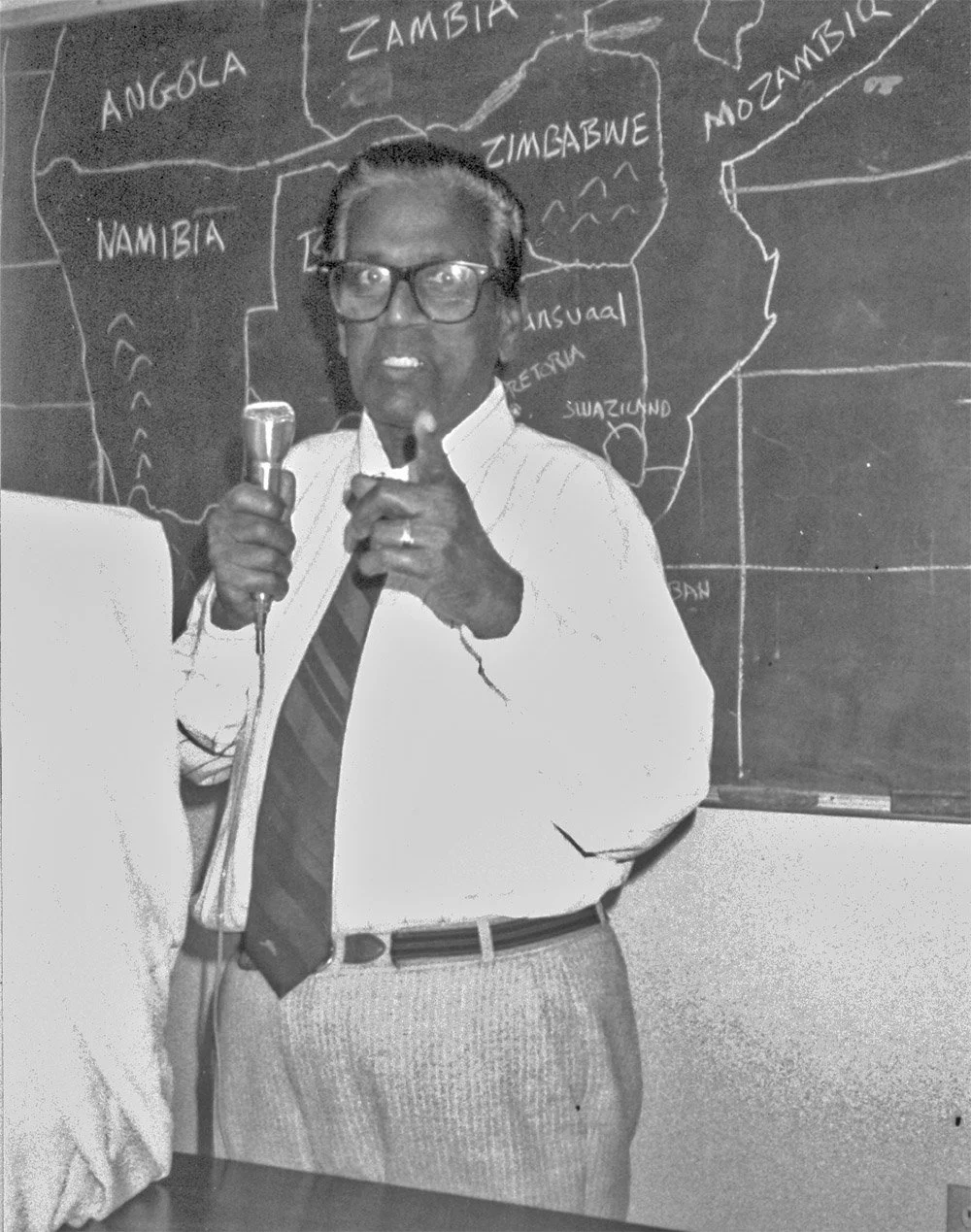 N.T. Naicker with microphone in front of map of Southern Africa