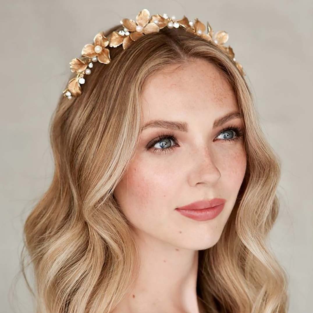 A woman with long wavy blonde hair wearing a floral headband with golden flowers and pearls.