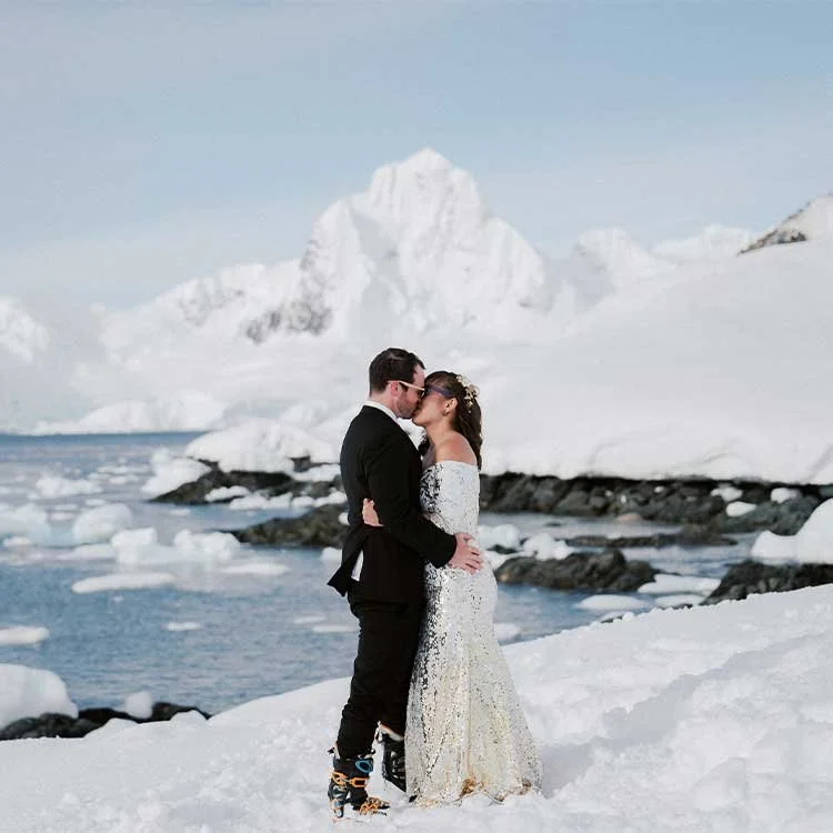 A newly married couple in a wintry environment near water and mountains