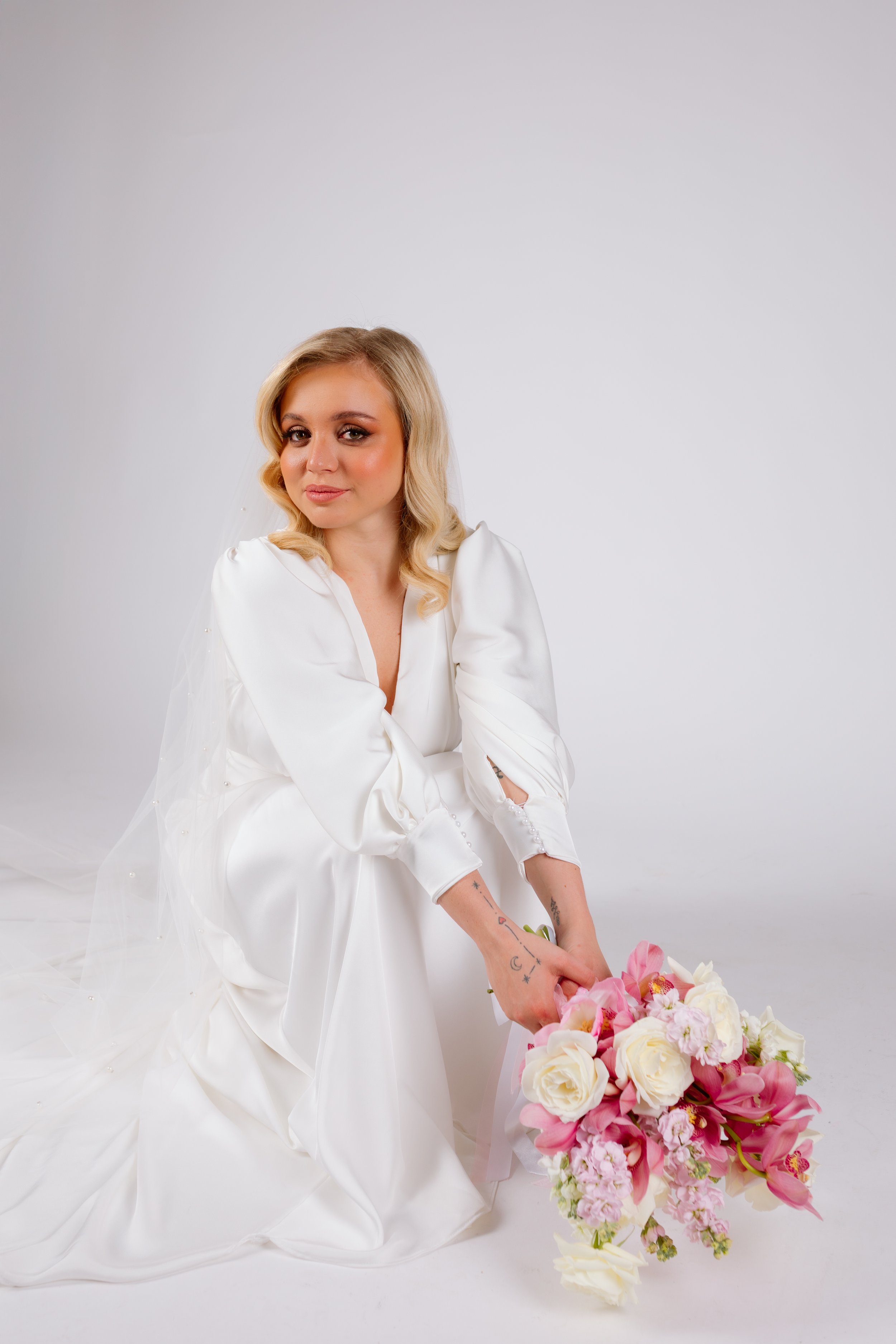 Editorial bridal portrait of a bride wearing soft glam wedding makeup and elegant bridal hairstyle, sitting with a pink bouquet. Natural bridal beauty by Rita Jacinto Makeup in Portugal for destination weddings.