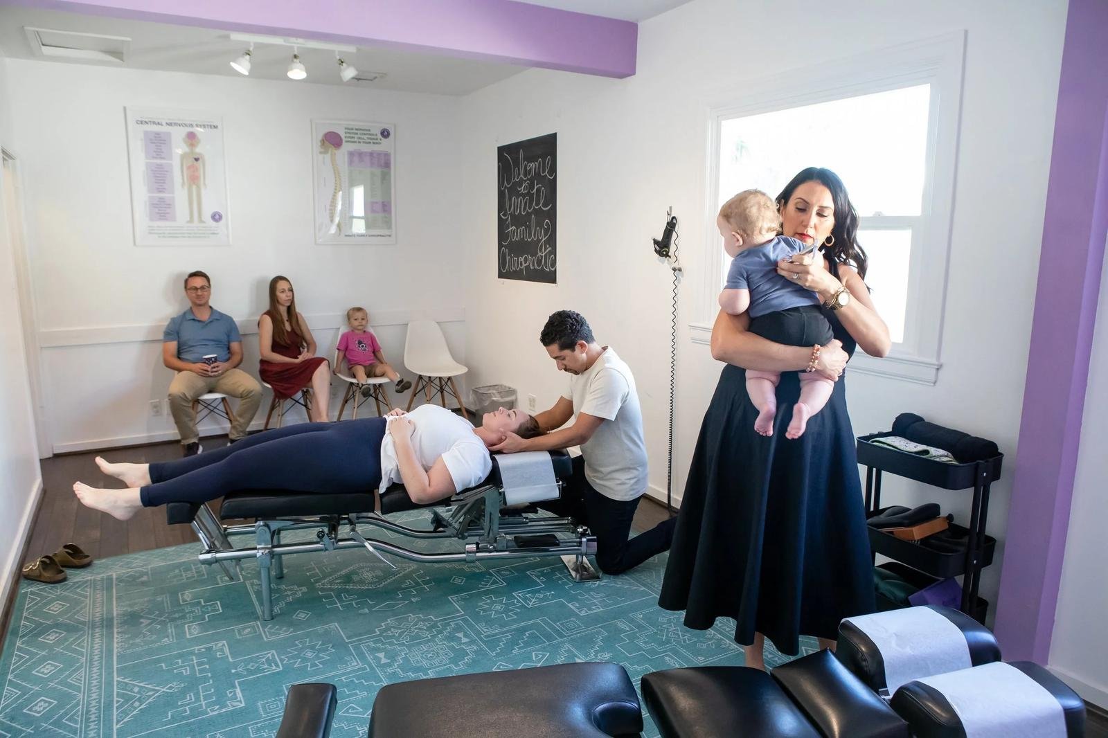 Family chiropractic care at Innate Family Chiropractic Pasadena CA — Dr. Adana holds an infant while a patient is adjusted.