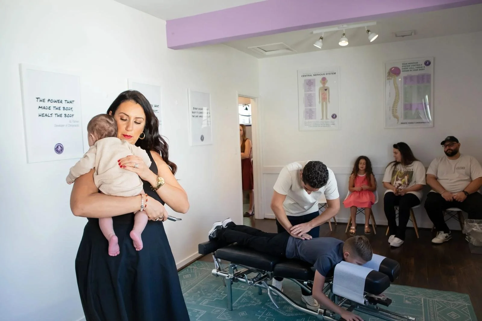 Dr. Adana Vargas of Innate Family Chiropractic Pasadena CA holding a newborn while a young patient is adjusted in the background.