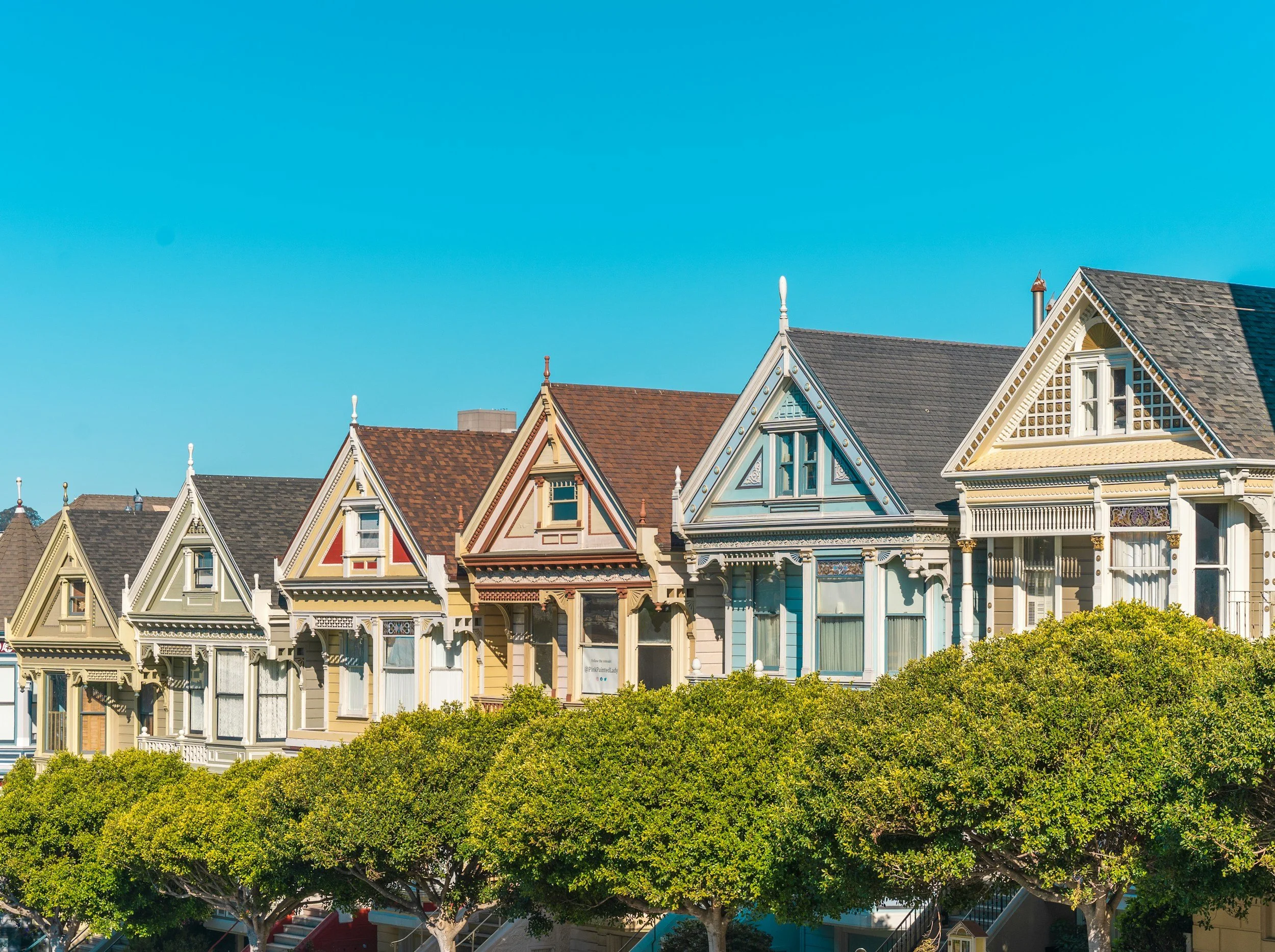 "Colorful Victorian-style residential homes featuring intricate woodwork and pointed rooftops, showcasing historic property styles by DillCo Development Group."