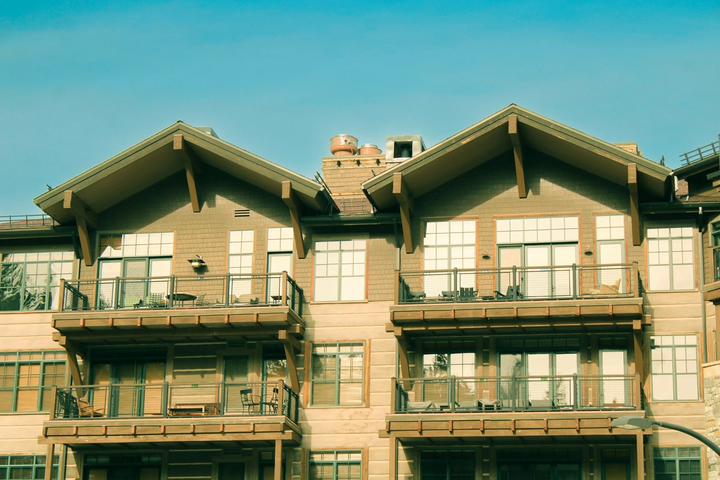 Multi-story residential building with balconies, large windows, and a roof with chimneys and vents, under a clear blue sky. DillCo Development Group