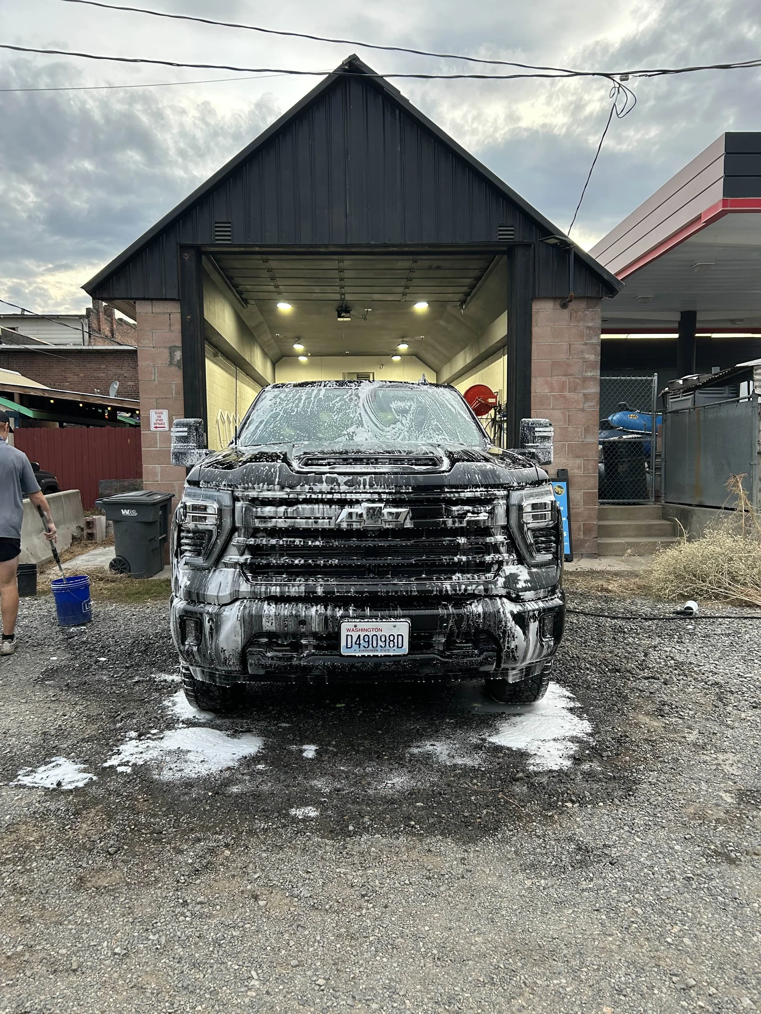 A black pickup truck being washed with soap suds in front of a car wash station.