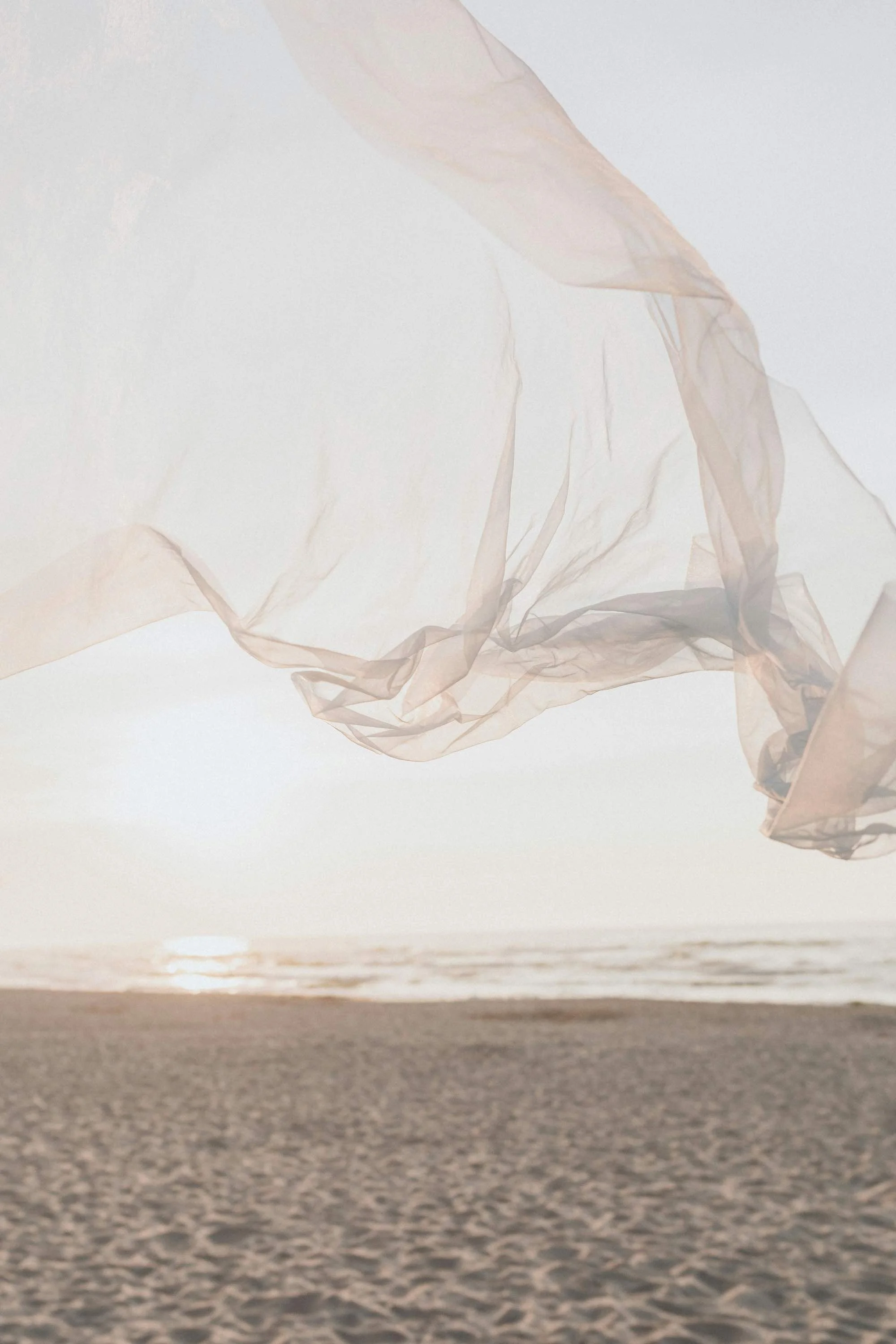 Beach scene during sunset with fabric blowing in the breeze and calm ocean in the background.