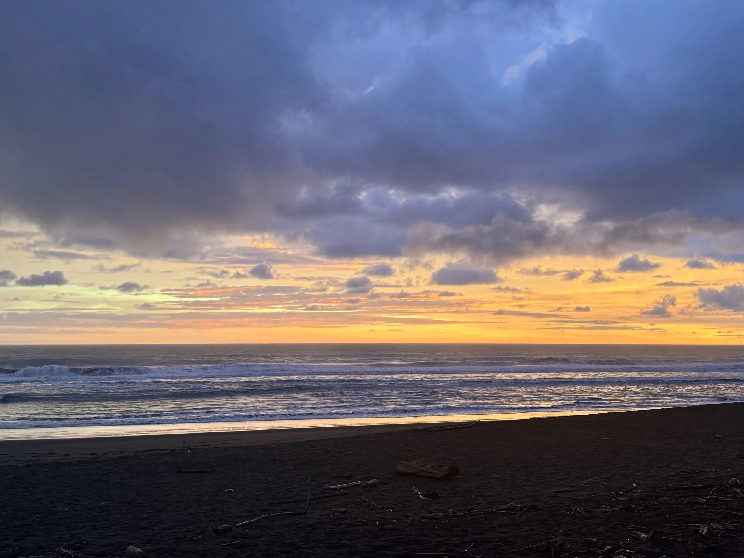 Ocean waves at Hermosa Beach under layered gray clouds glowing with orange and yellow sunset light.