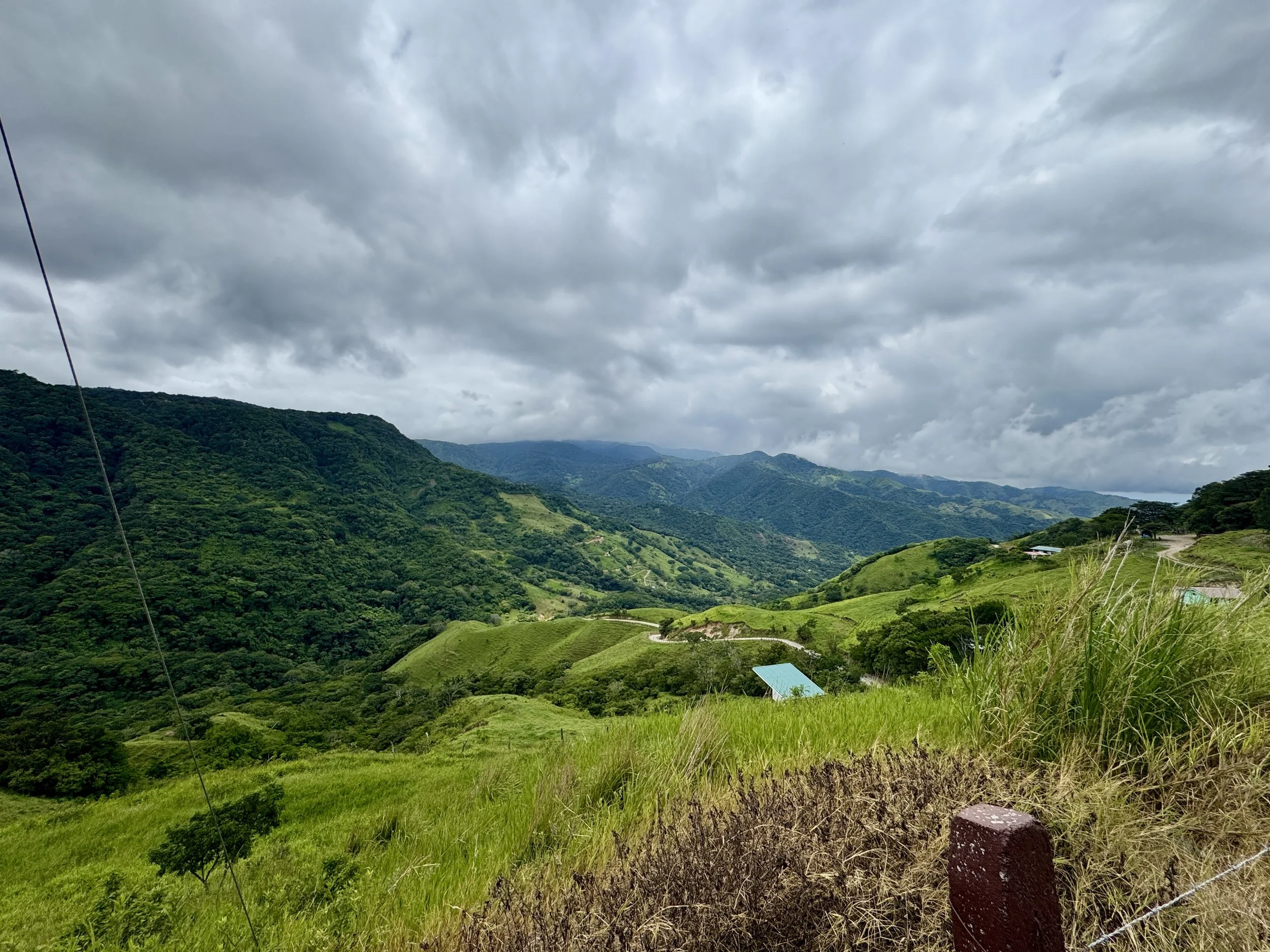 Expansive countryside with bright green hills and a small lake in the distance, captured after pulling over along the mountain road.