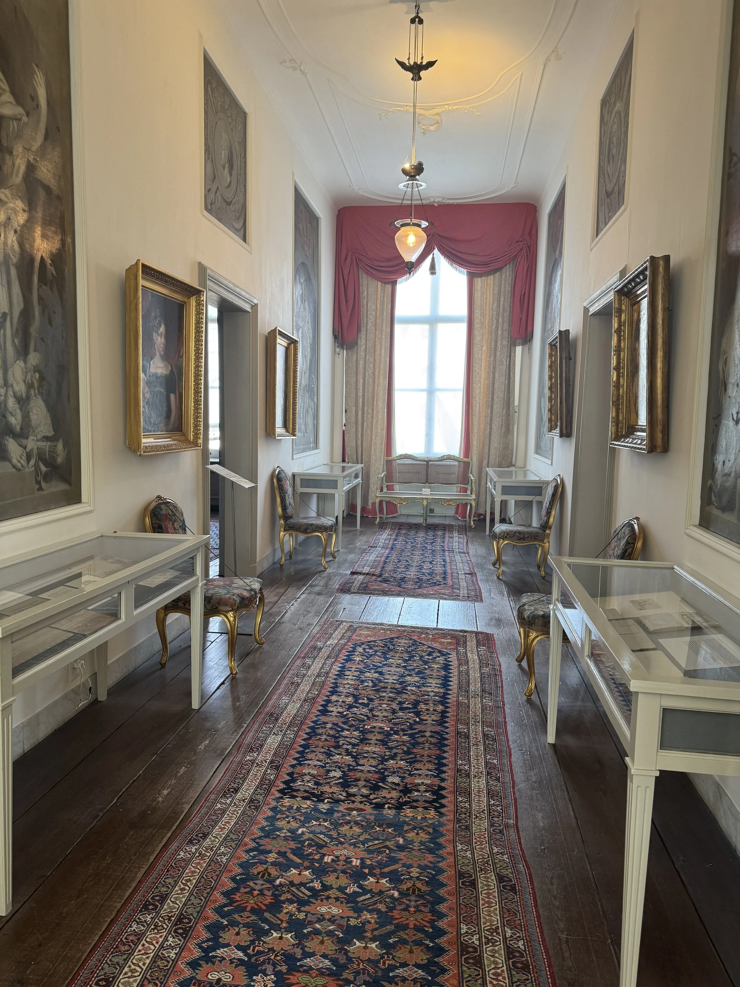 Long hallway with framed artwork and patterned rug inside Museum Van Loon in Amsterdam