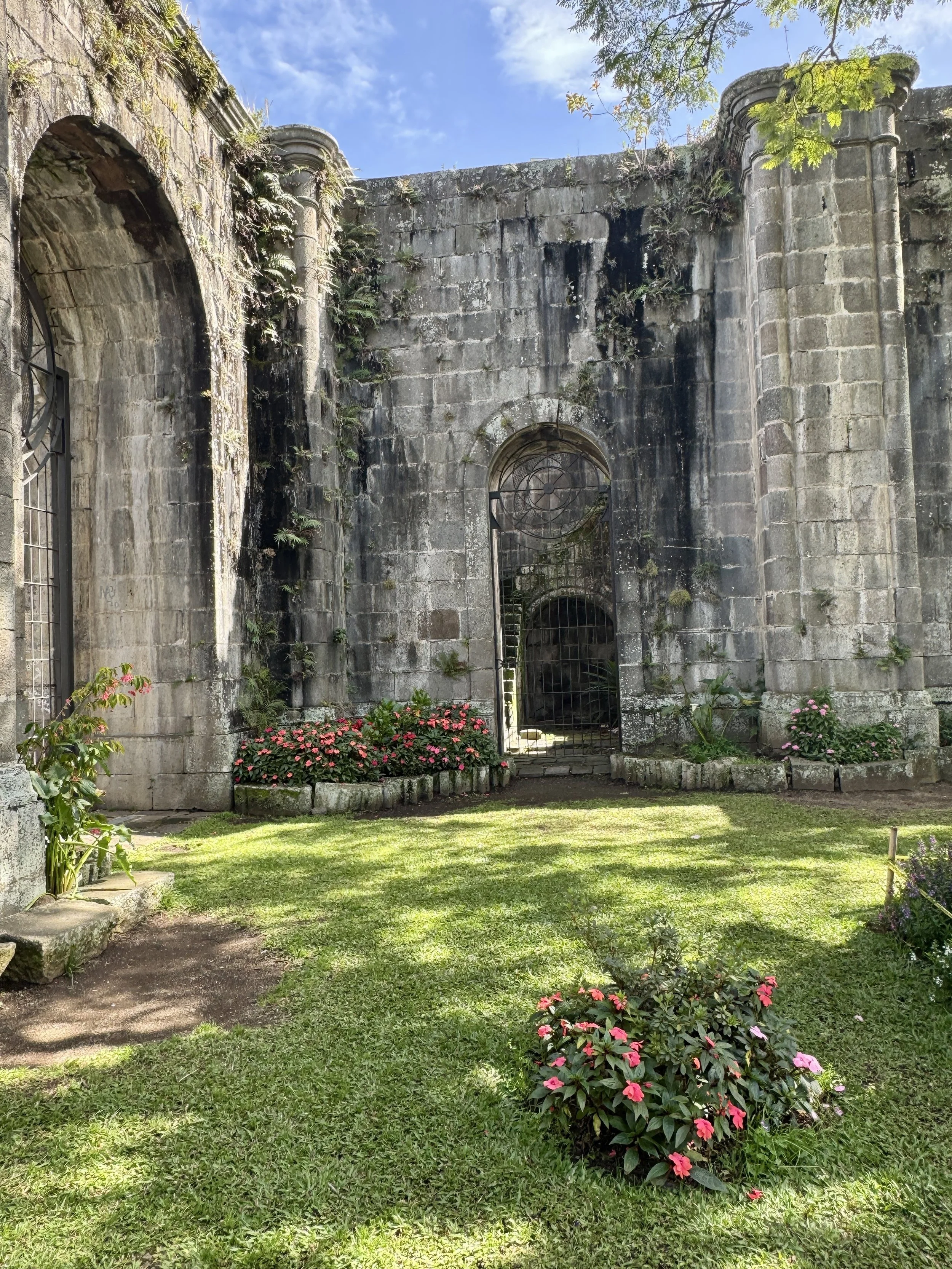 Historic stone walls and arched windows of the Santiago Apóstol church ruins surrounded by lawn and flowers.