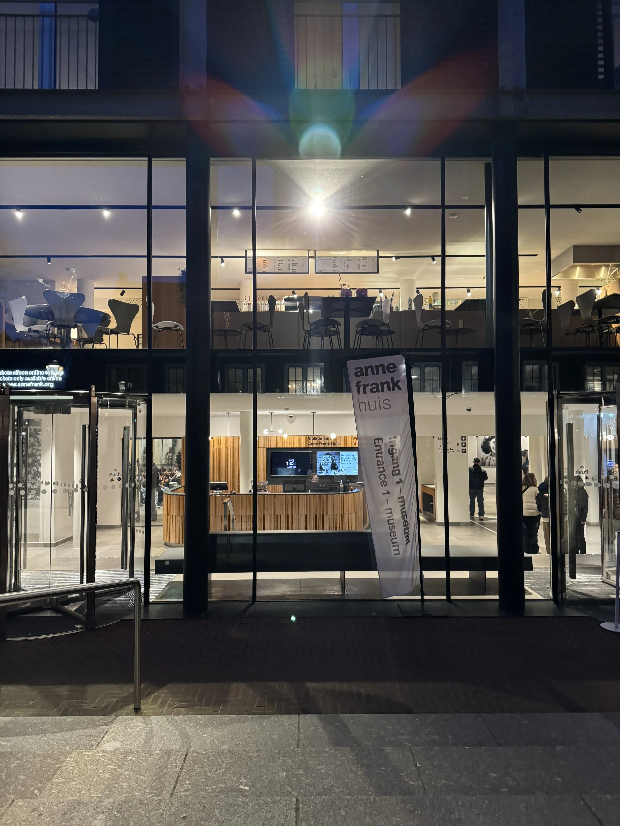 Exterior entrance of the Anne Frank House museum in Amsterdam at night with illuminated glass facade