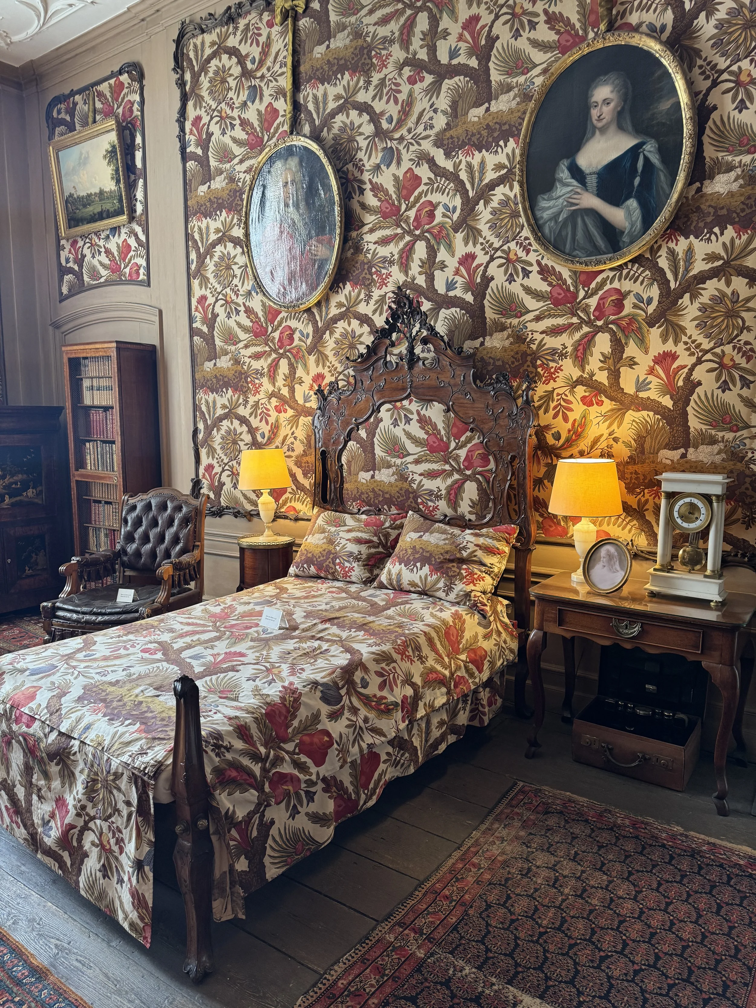 Ornate bedroom with patterned wallpaper, antique bed, and portraits at Museum Van Loon Amsterdam