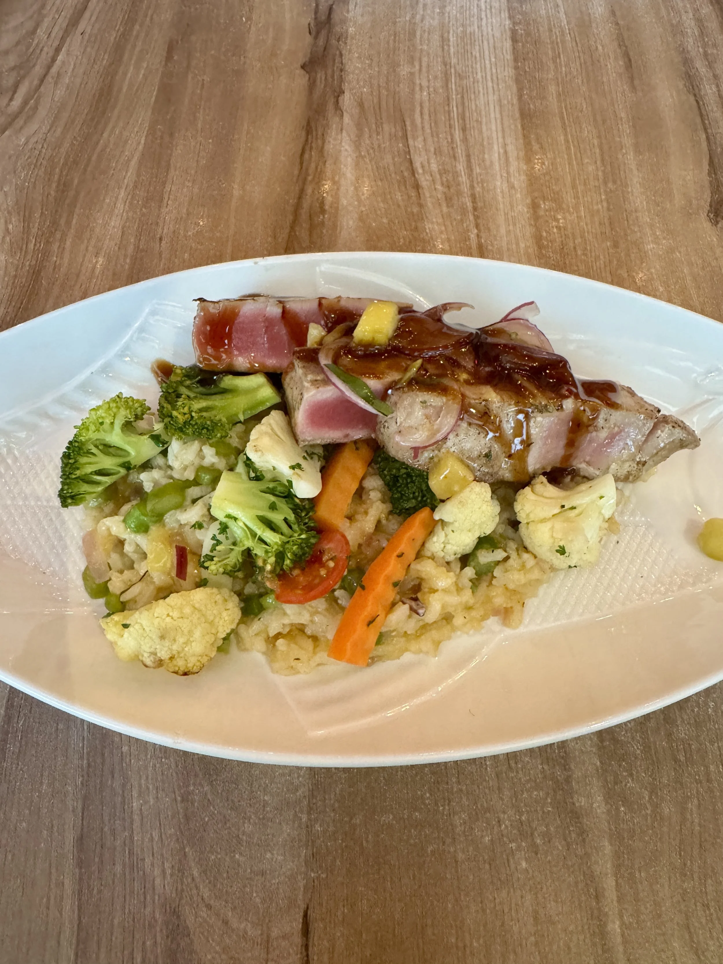 Plated ahi tuna with mixed vegetables and asparagus risotto served on a white dish.