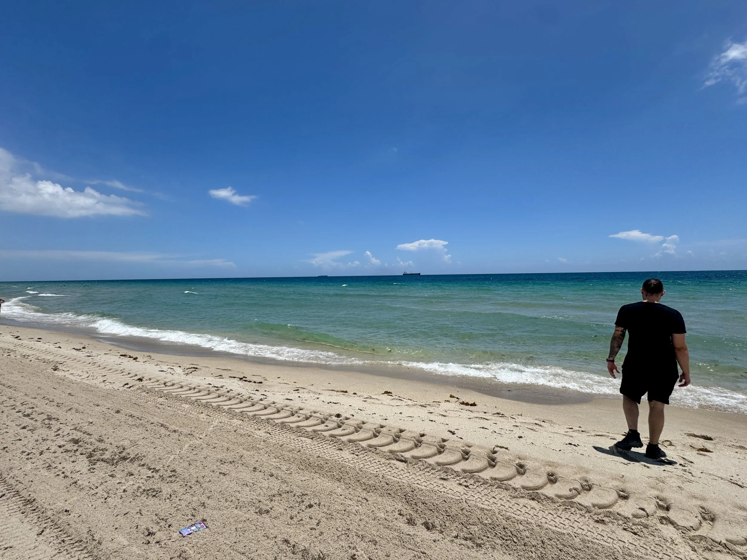 person walking along the sandy beach shoreline with turquoise water in Fort Lauderdale