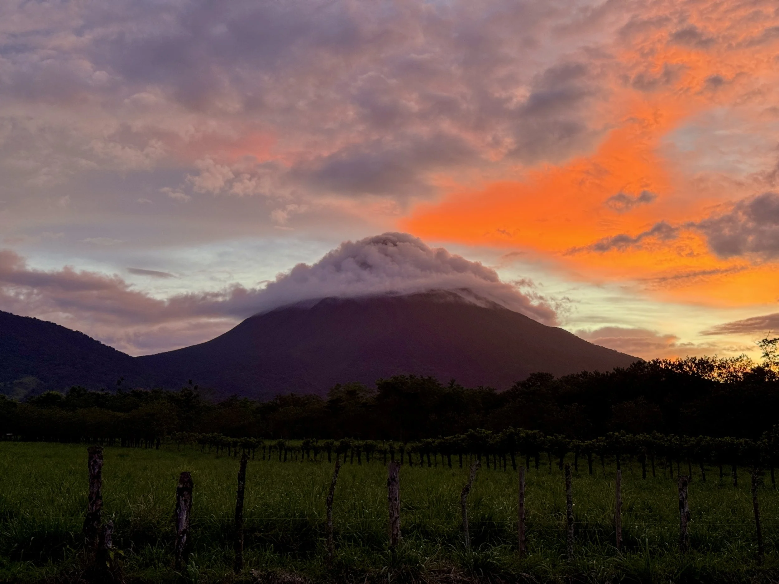 Arenal Volcano silhouetted at sunset with dramatic orange and pink clouds over La Fortuna.
