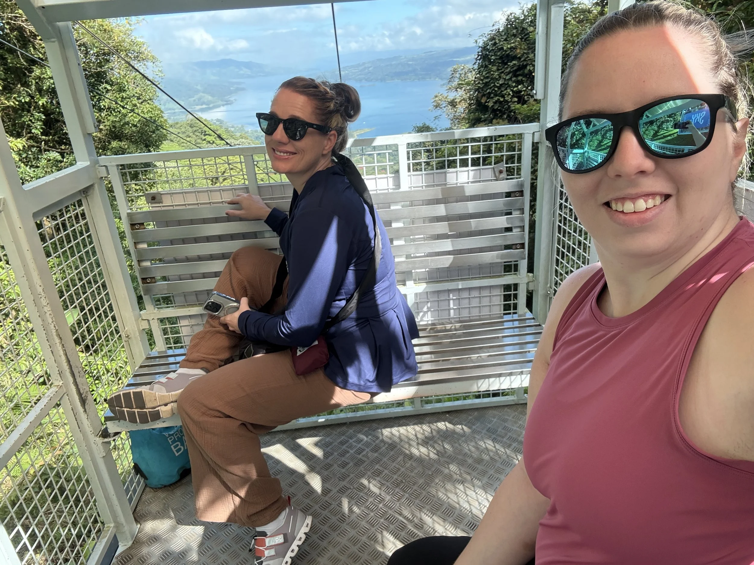 Two visitors riding the Sky Adventures tram with rainforest and lake views in the background.