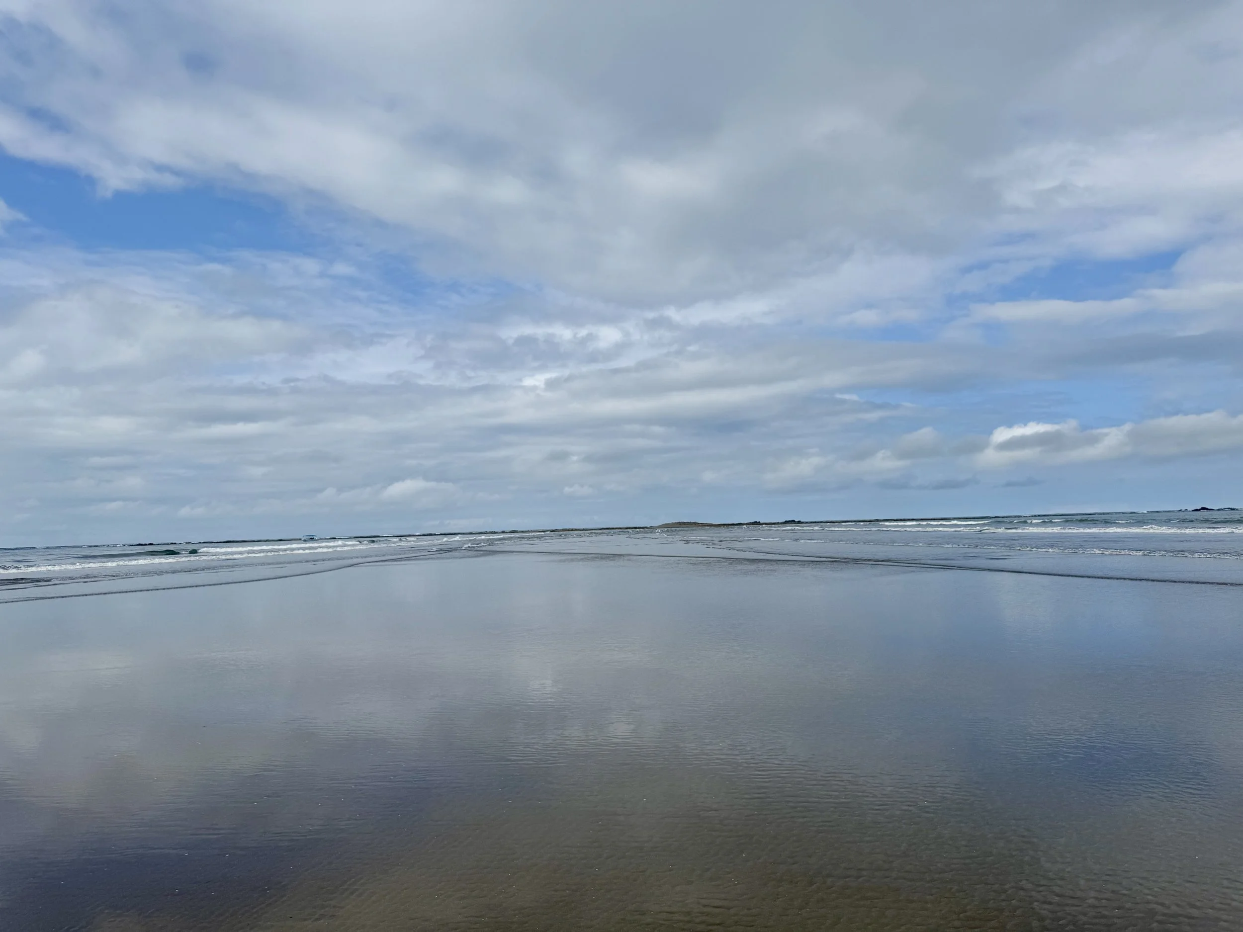 Calm ocean water reflecting blue sky and clouds along the whale tail sandbar.