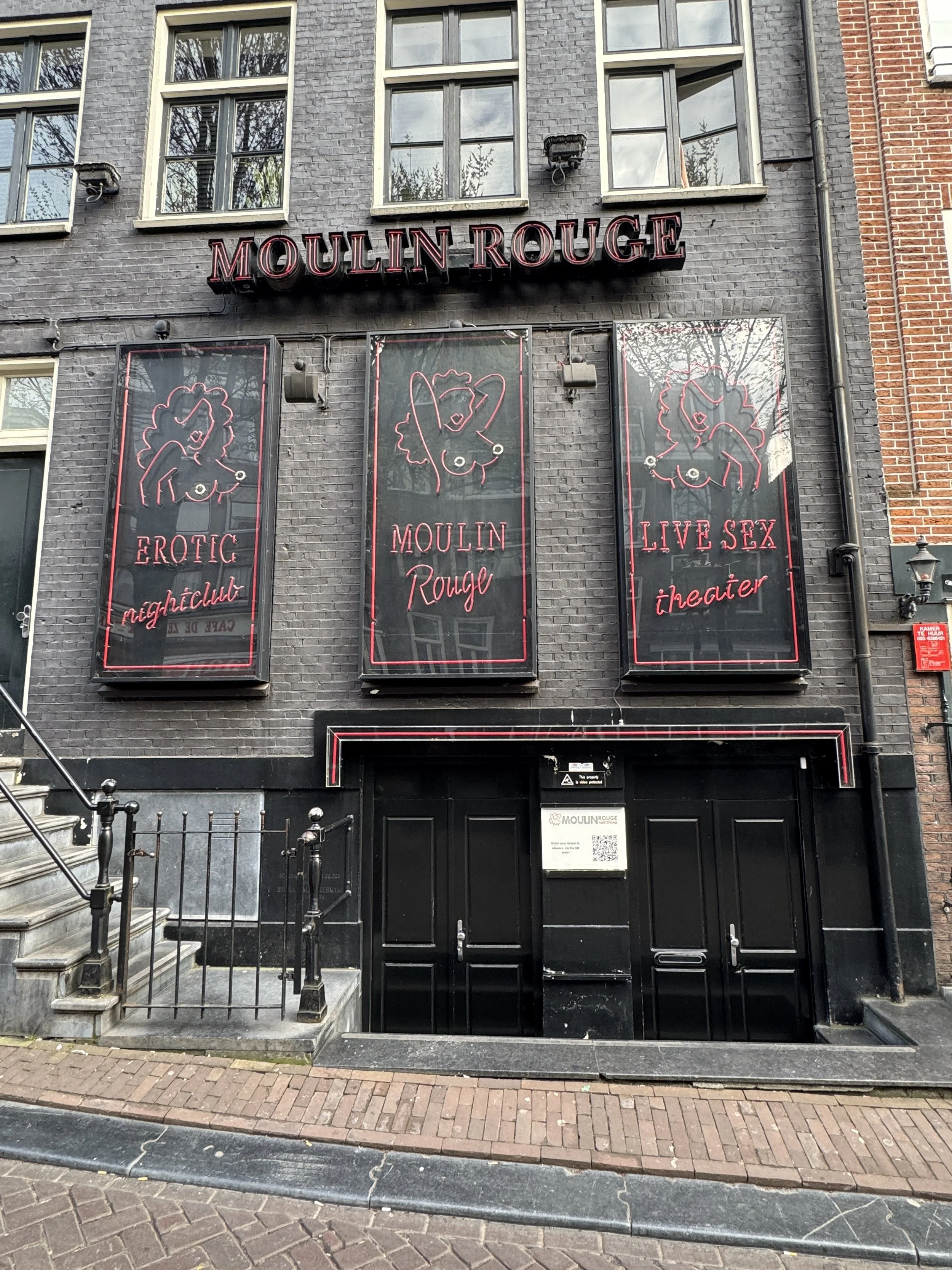 Exterior of a building in Amsterdam’s Red Light District with illuminated windows and signage